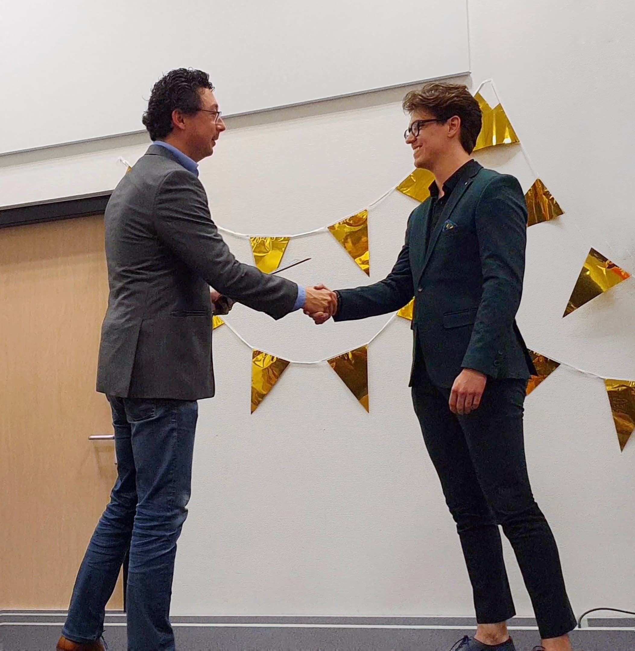 Rick van de Sande schudt de hand met zijn begelider Misha Croes, die hem feliciteert met zijn diploma.